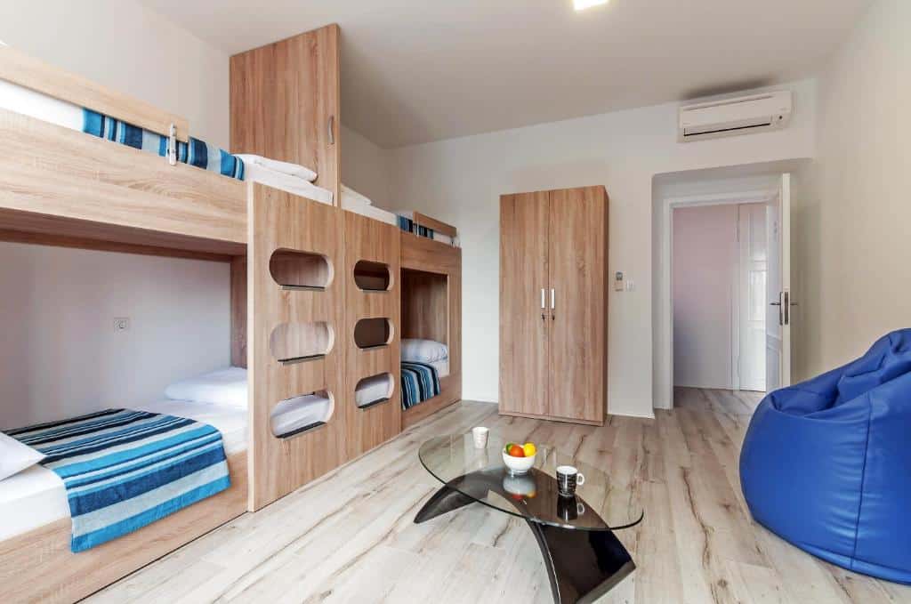 Quarto partilhado com beliche de madeira, cacifo e pufe azul num hostel moderno, no Sky Hostel (Kolovare)