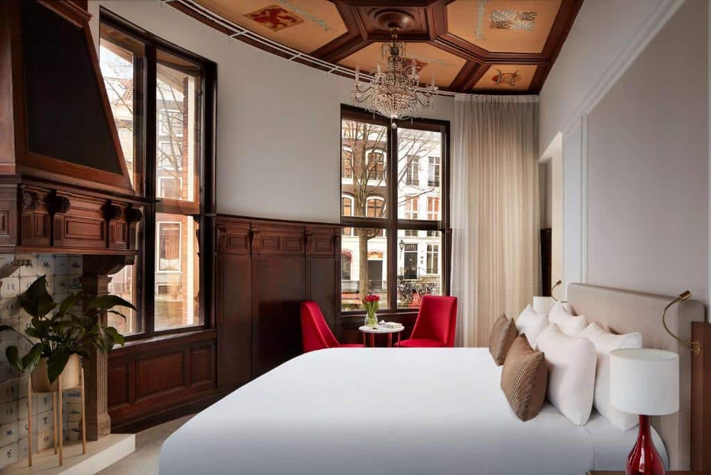 Quarto do Tivoli Doelen Amsterdam Hotel, que ilustra onde ficar em Amesterdão: cama grande, duas cadeiras vermelhas junto a uma janela, paredes com painéis de madeira e um teto decorativo.