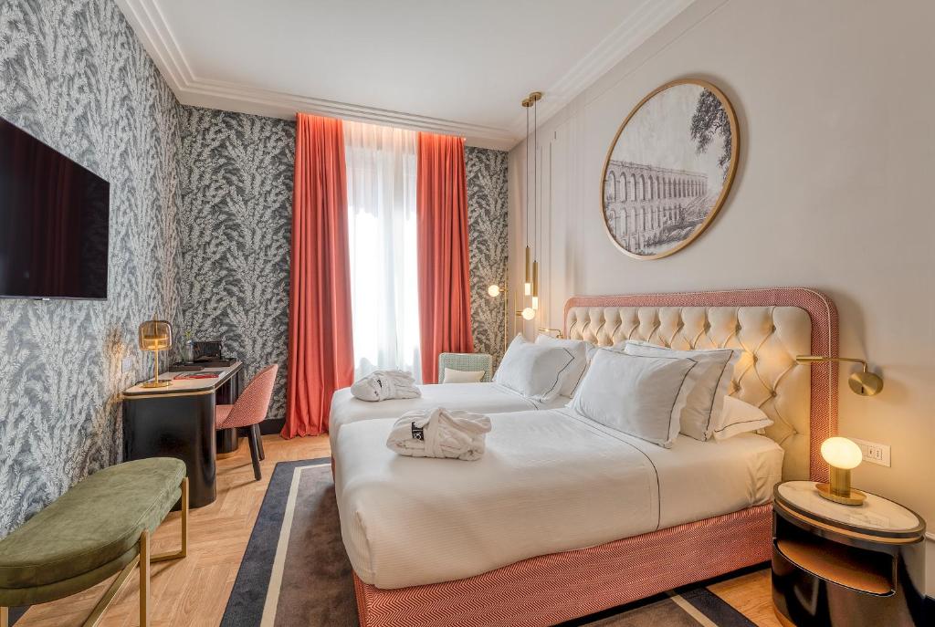 quarto do H10 Palazzo Galla, um dos hotéis no centro de Roma, com cama de casal grande, espelho redondo por cima, mesa com poltrona e televisão em frente, papel de parede monocromático em cinza com pormenores em rosa claro e uma janela comprida com cortinas