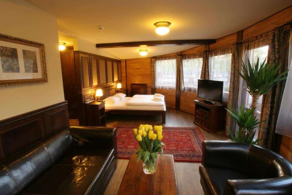 Quarto do Boat Hotel Matylda, com cama de casal, sofás de couro, uma TV, janelas grandes e túlipas amarelas numa mesa de madeira.