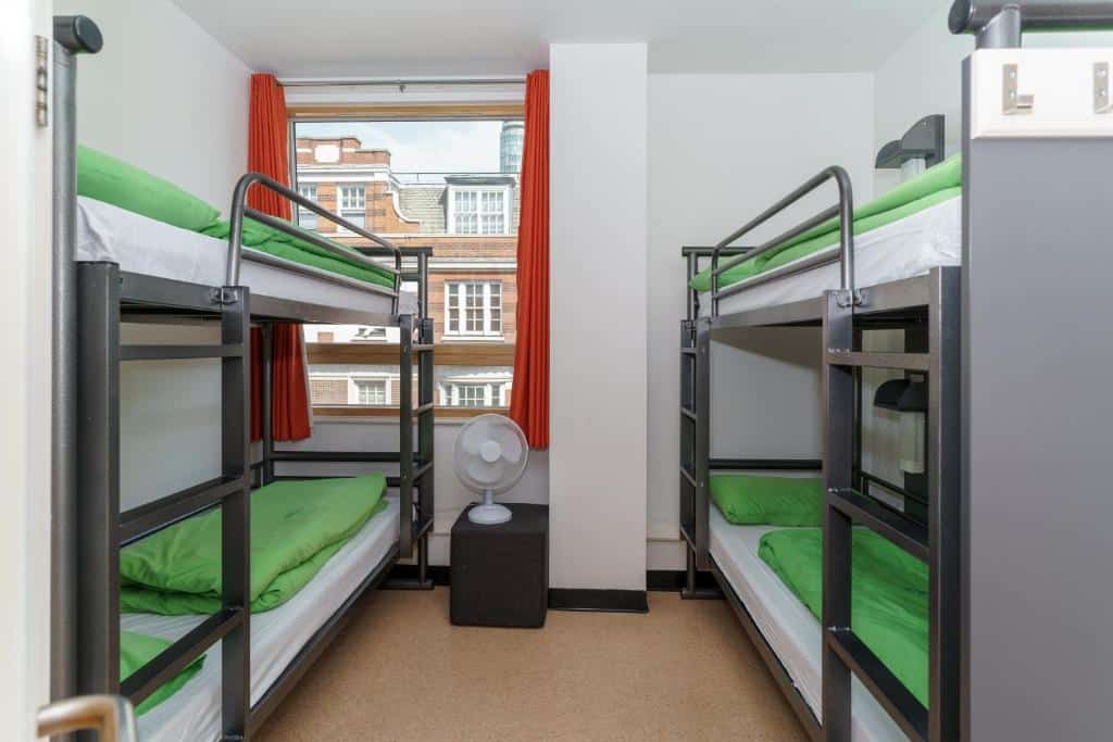 Quarto partilhado do YHA London Central com dois beliches, uma janela com cortinas e uma ventoinha de chão.