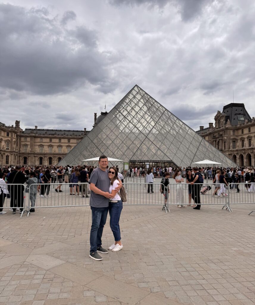 Um casal em frente à entrada da pirâmide de vidro do Museu do Louvre, em Paris