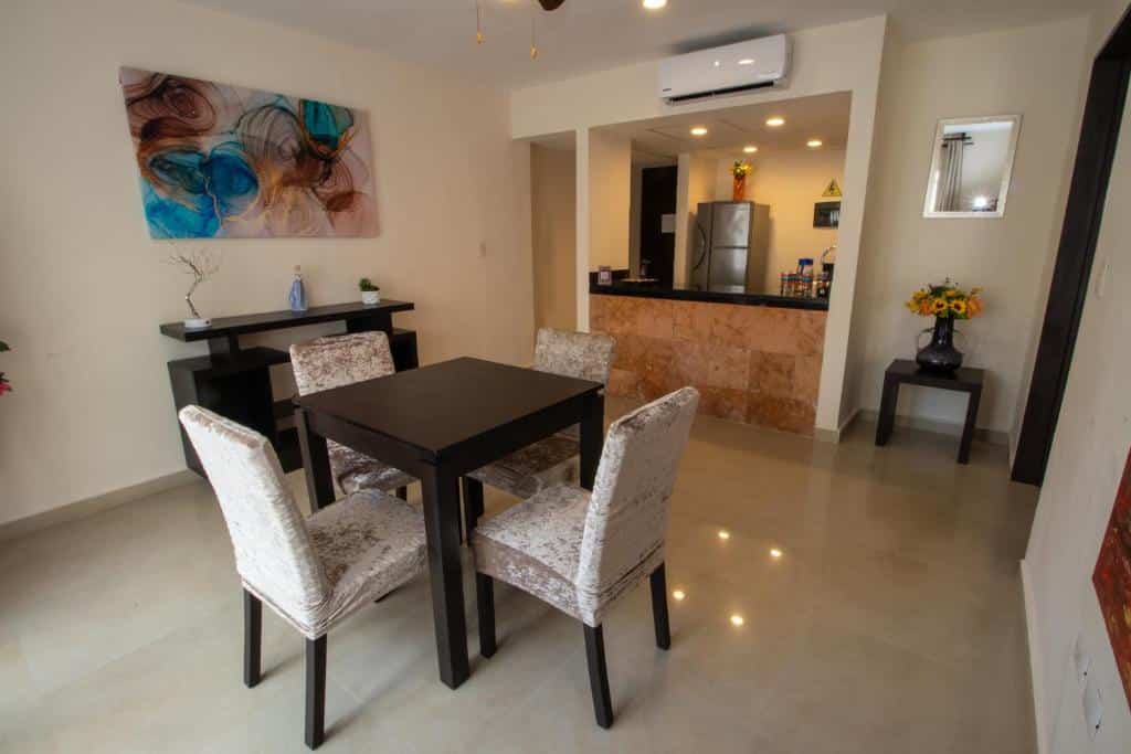 Sala de jantar moderna com mesa escura e quatro cadeiras estofadas em tons de bege, integrada na cozinha aberta do Hotel Villas Segovia Playa del Carmen.
