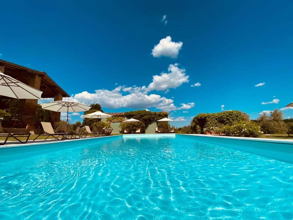 Piscina da Ca’ Bianca, um dos hotéis na Toscana, com água azul, poltronas e chapéus de sol ao lado, além de flores e relvado verde