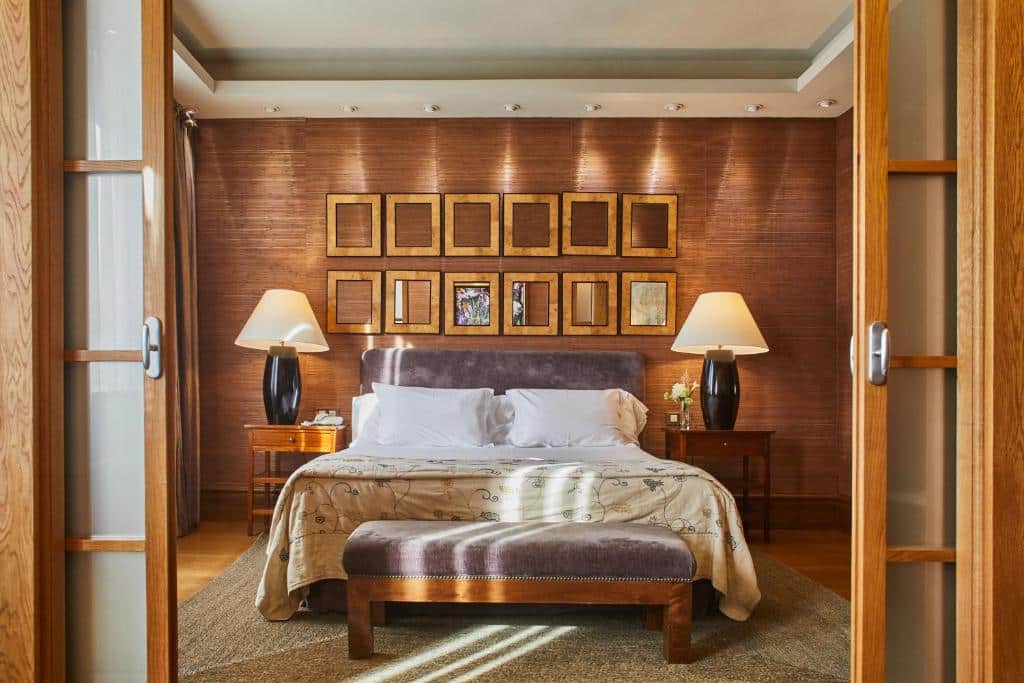 Quarto do Silken Al-Andalus Palace com cama de casal, um candeeiro de cada lado e um banco estofado aos pés da cama.