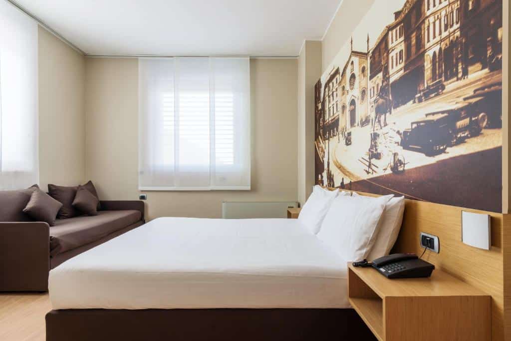 Quarto com cama de casal, sofá, janela e mobiliário em madeira no B&B Hotel Milano La Spezia