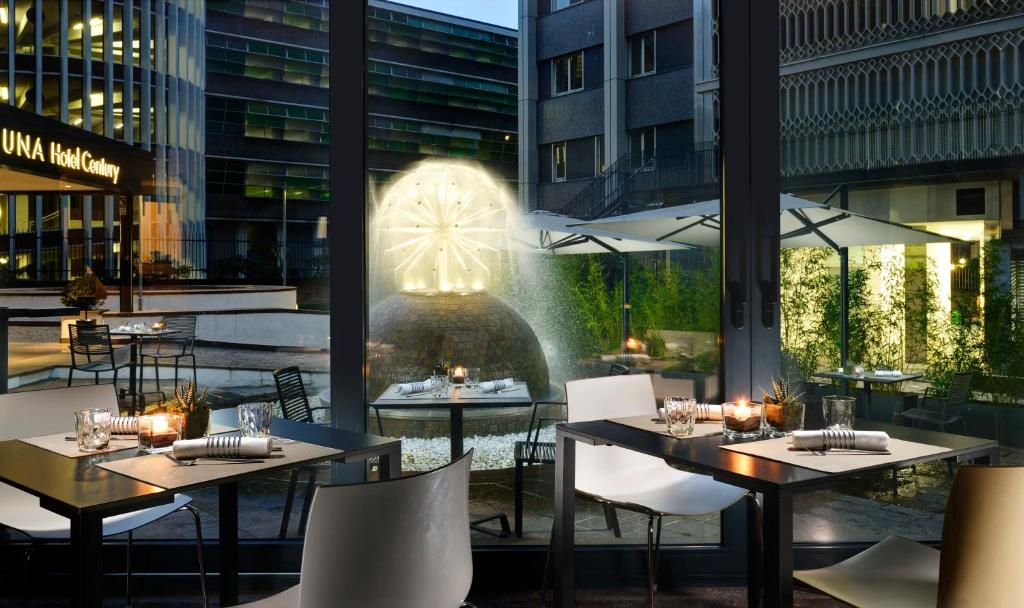 Sala de refeições do UNAHOTELS Century Milano com portas de vidro com vista para uma fonte iluminada rodeada de plantas