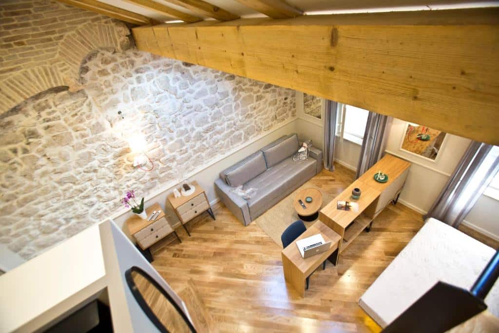 Quarto de hotel acolhedor com sofá cinzento, secretária e parede de pedra rústica, no Borelli Palace & Borelli Blue, na Cidade Velha