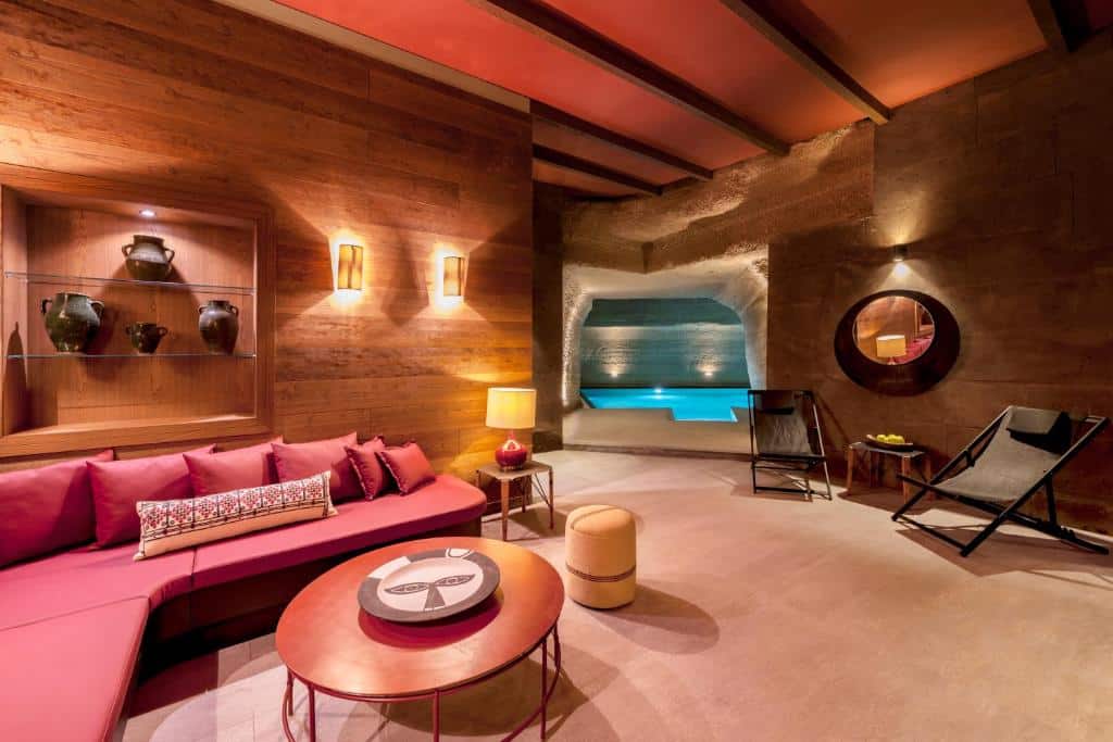 Zona de lounge moderna do Carus Cappadocia, um dos hotéis da Capadócia, com sofá vermelho, paredes de madeira, arte na parede e vista para uma piscina interior através de uma abertura em forma de caverna.