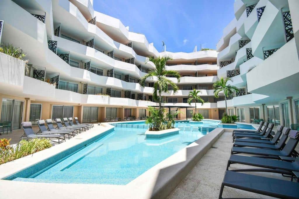 Piscina azul no The Gallery Condos Playa del Carmen com espreguiçadeiras, palmeiras e arquitetura moderna.