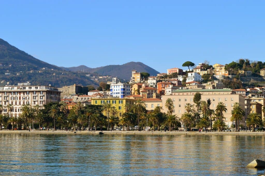 Edifícios coloridos junto à marina de La Spezia, com palmeiras e barcos numa paisagem soalheira