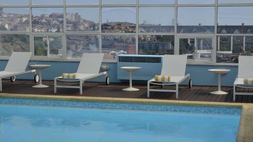 Zona de piscina na cobertura do Hotel Mercure Lisboa, com espreguiçadeiras brancas e vista para a paisagem urbana.