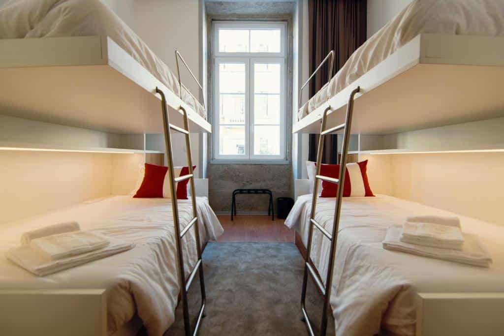 Dormitório com dois beliches, roupa de cama branca e almofadas vermelhas, no HI Braga – Pousada de Juventude.
