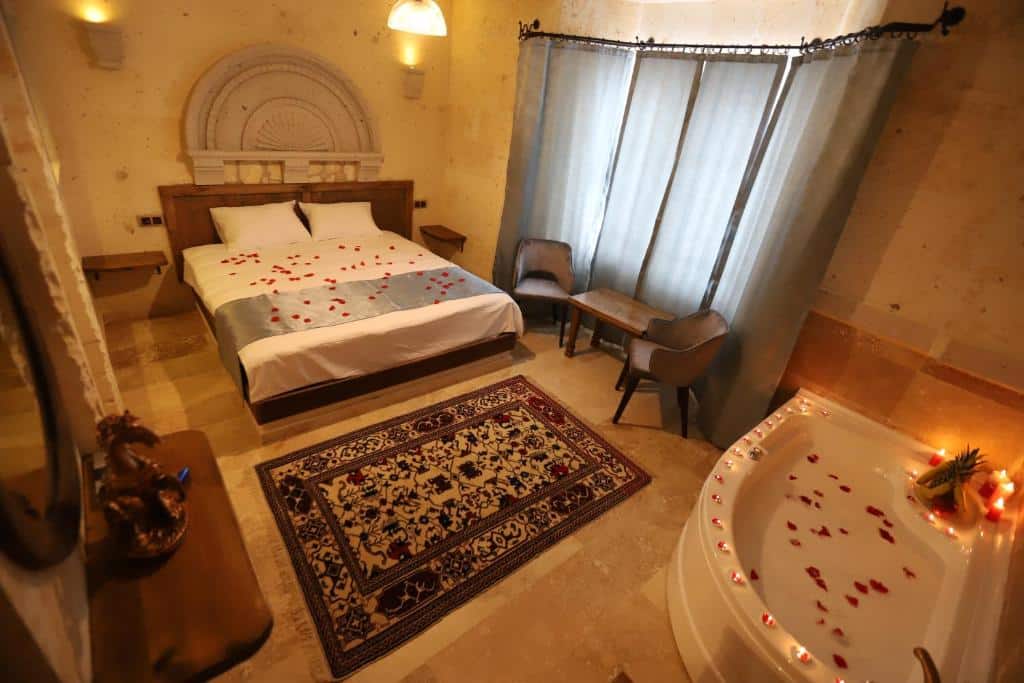 Quarto do Castle Panorama House com cama de casal, tapete, duas cadeiras, mesa, banheira de hidromassagem e pétalas de rosa espalhadas pelas superfícies.