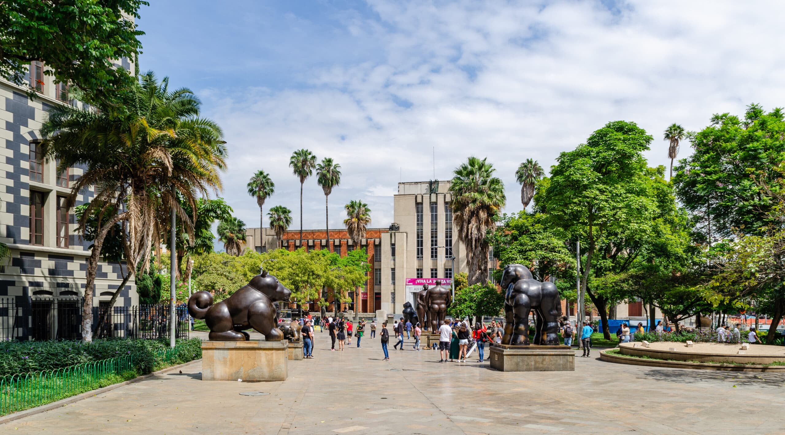 Plaza Botero com duas grandes esculturas de animais rodeadas de palmeiras e pessoas a passear num dia de sol.