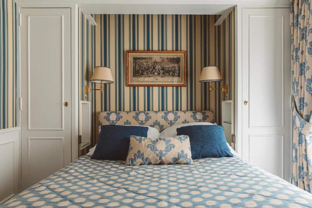 Cama bem composta no Hôtel de l'Abbaye, com roupa de cama em tons de azul e bege, num quarto com papel de parede às riscas.