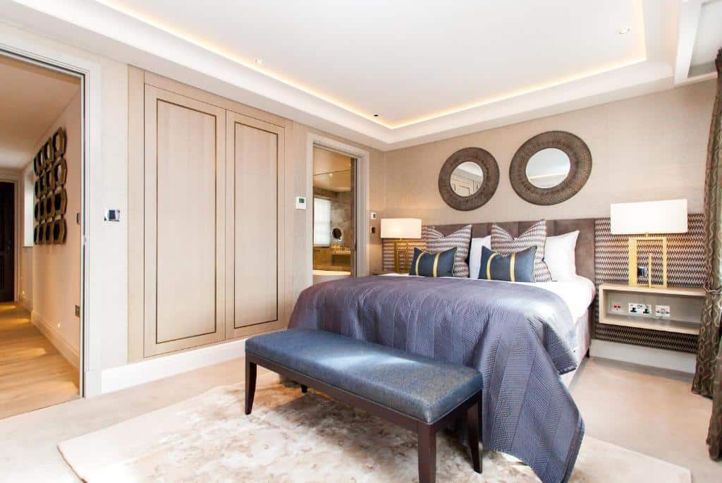 Quarto de luxo do Hope House Residences by Q Apartments com cama de casal, dois espelhos redondos, duas mesas de cabeceira com candeeiros, um pequeno armário, um tapete e um sofá.