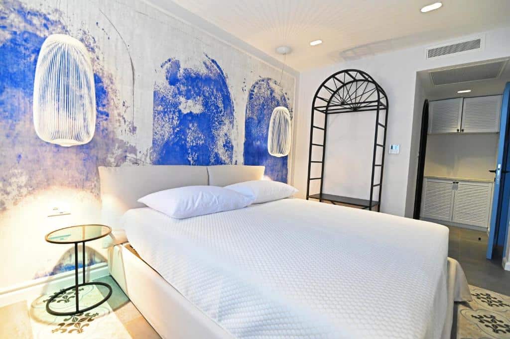 Quarto de hotel moderno com cama de casal branca, parede azul texturada e candeeiros suspensos, no Borelli Palace & Borelli Blue