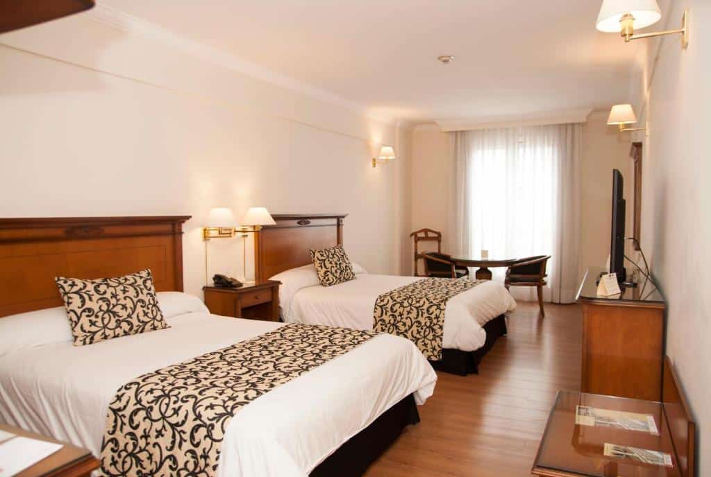 quarto do Scala Hotel Buenos Aires com duas camas de casal, mesa com candeeiro entre elas, janela grande com cortinas e uma secretária