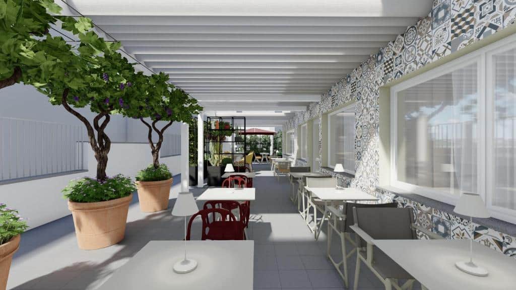 área comum do Adesso Hotel com mesas brancas e cadeiras de madeira de um lado e de ferro em tons de vermelho do outro, com papel de parede, vasos grandes de plantas verdes e, ao fundo, cadeirões e mais vasos de plantas