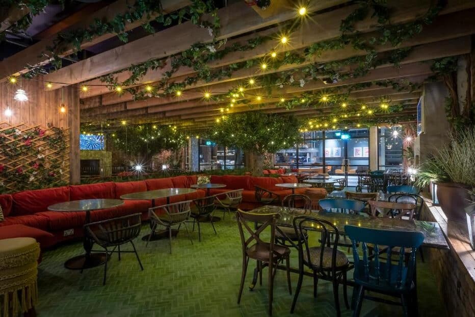 Esplanada do restaurante do Marlin Hotel Stephens Green com decoração rústica, cadeiras coloridas e fios de luzes suspensos entre treliças de madeira cobertas de plantas.