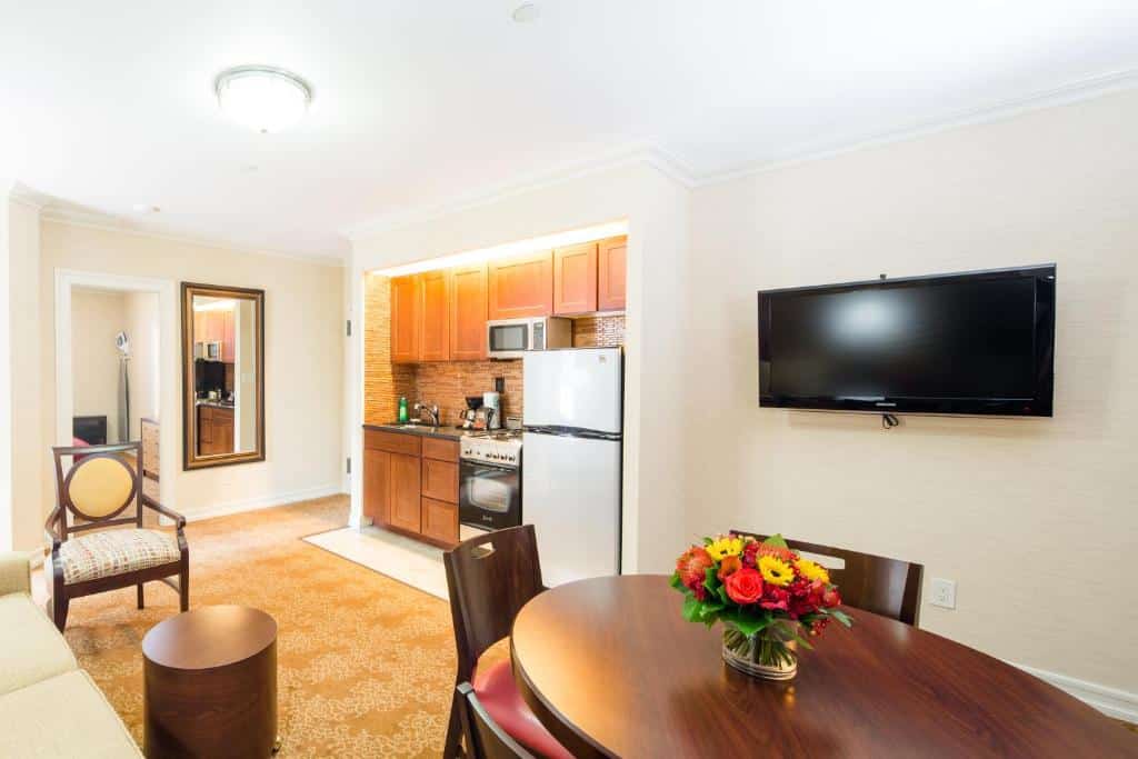 Sala e cozinha integradas do Radio City Apartments, com uma mesa redonda de madeira à direita, por baixo de uma TV de parede. À esquerda, uma pequena cozinha com armários de madeira, lava-loiça, micro-ondas, máquina de café, fogão a gás e frigorífico.