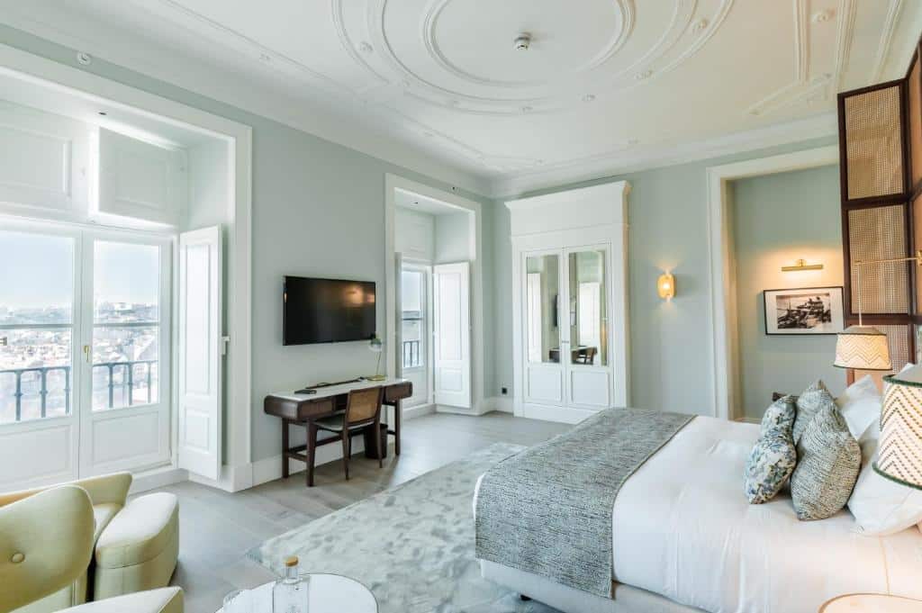Quarto de luxo do Palácio Ludovice Wine Experience Hotel, com duas varandas e uma televisão e secretária entre elas, um armário com espelhos, poltronas estofadas e uma cama de casal ao centro