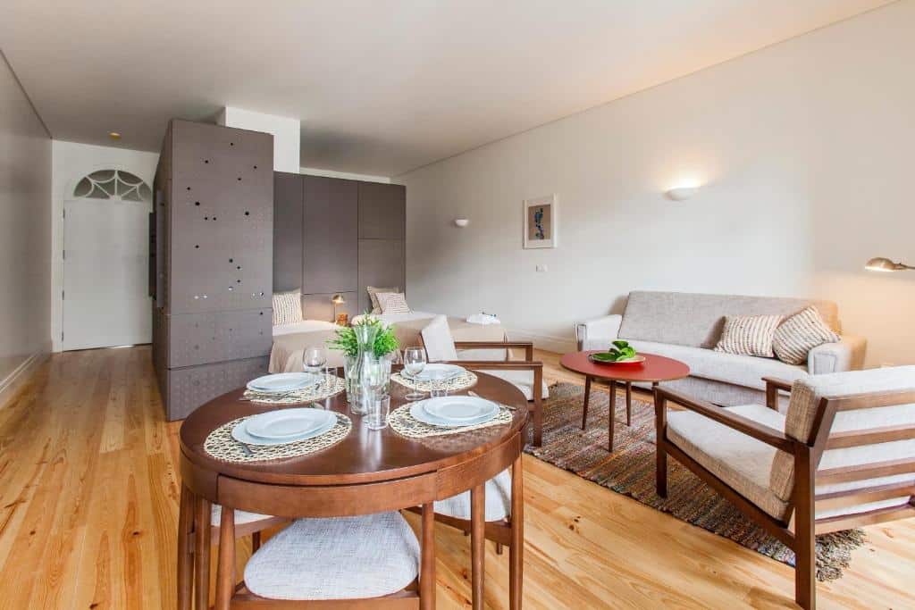 Sala de estar do bnapartments Loftpuzzle, com mesa redonda de madeira em primeiro plano, duas poltronas, um sofá e, ao fundo, duas camas de solteiro.