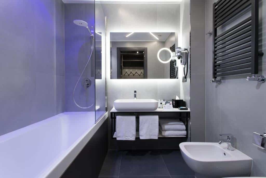Casa de banho do iQ Hotel Milano com banheira, espelho grande, lavatório com toalhas brancas e sanita