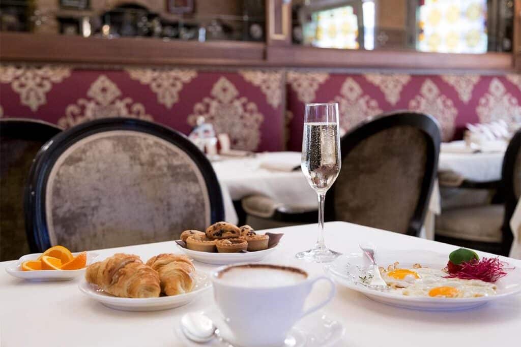 Copos de champanhe, pastelaria e um prato com salada numa mesa acolhedora de um restaurante com detalhes em vermelho e dourado