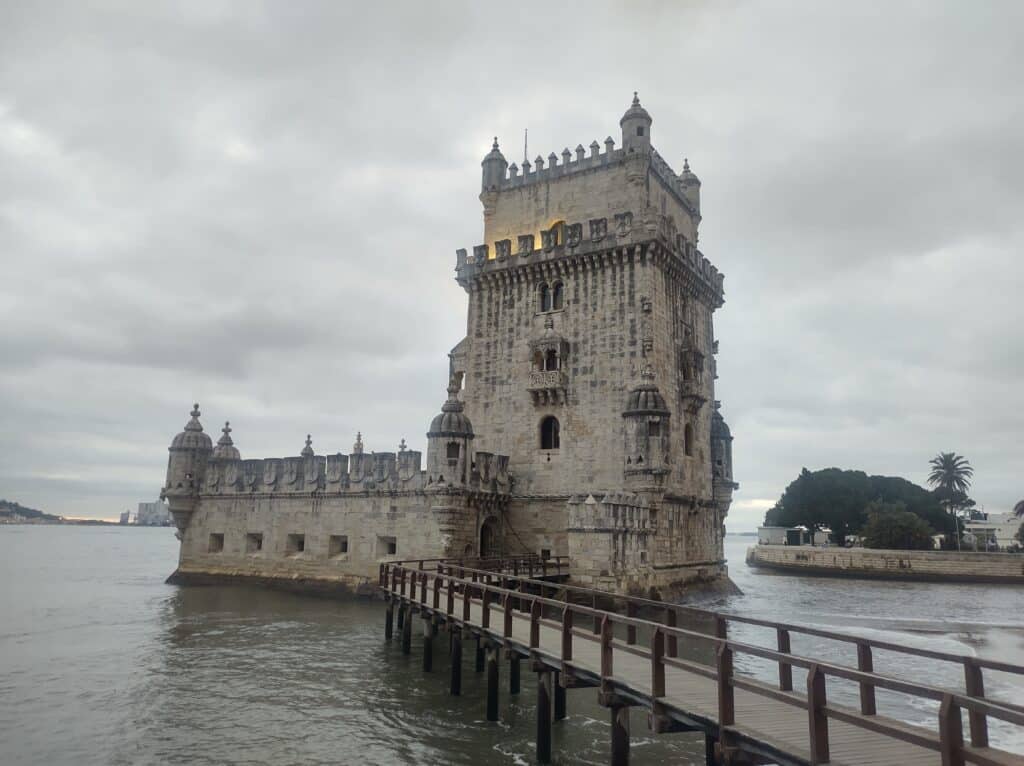 Imagem da Torre de Belém ao centro, durante o dia.