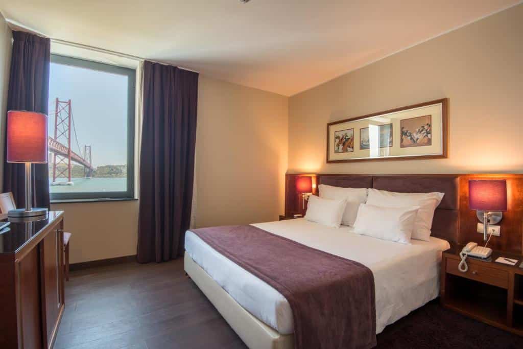 Quarto do Vila Gale Opera com cama de casal, candeeiros de cabeceira, janela com vista para a ponte e arte emoldurada