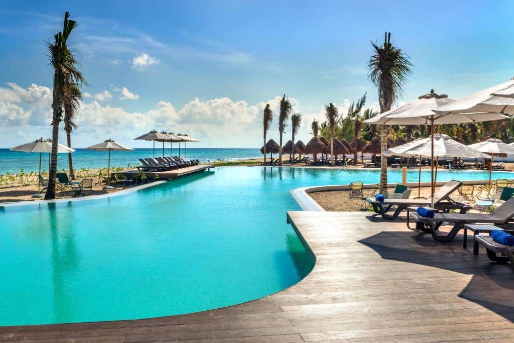 Piscina de bordo infinito no Ocean Riviera Paradise com tudo incluído, com espreguiçadeiras e chapéus de sol brancos.