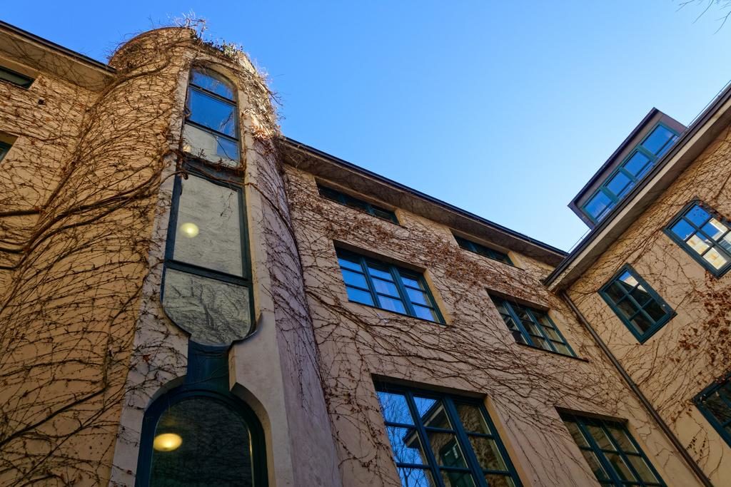 Edifício bege do Jugendherberge Wien – Myrthengasse, com janelas de acabamento verde e hera a subir pelas paredes, sob um céu azul.
