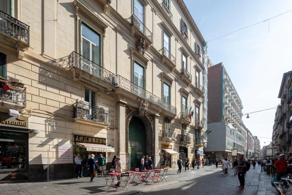 Fachada de edifício histórico com janelas e varandas no centro da cidade, pessoas a caminhar no passeio e mesas de café na rua, no Napolit'amo Hotel Principe.