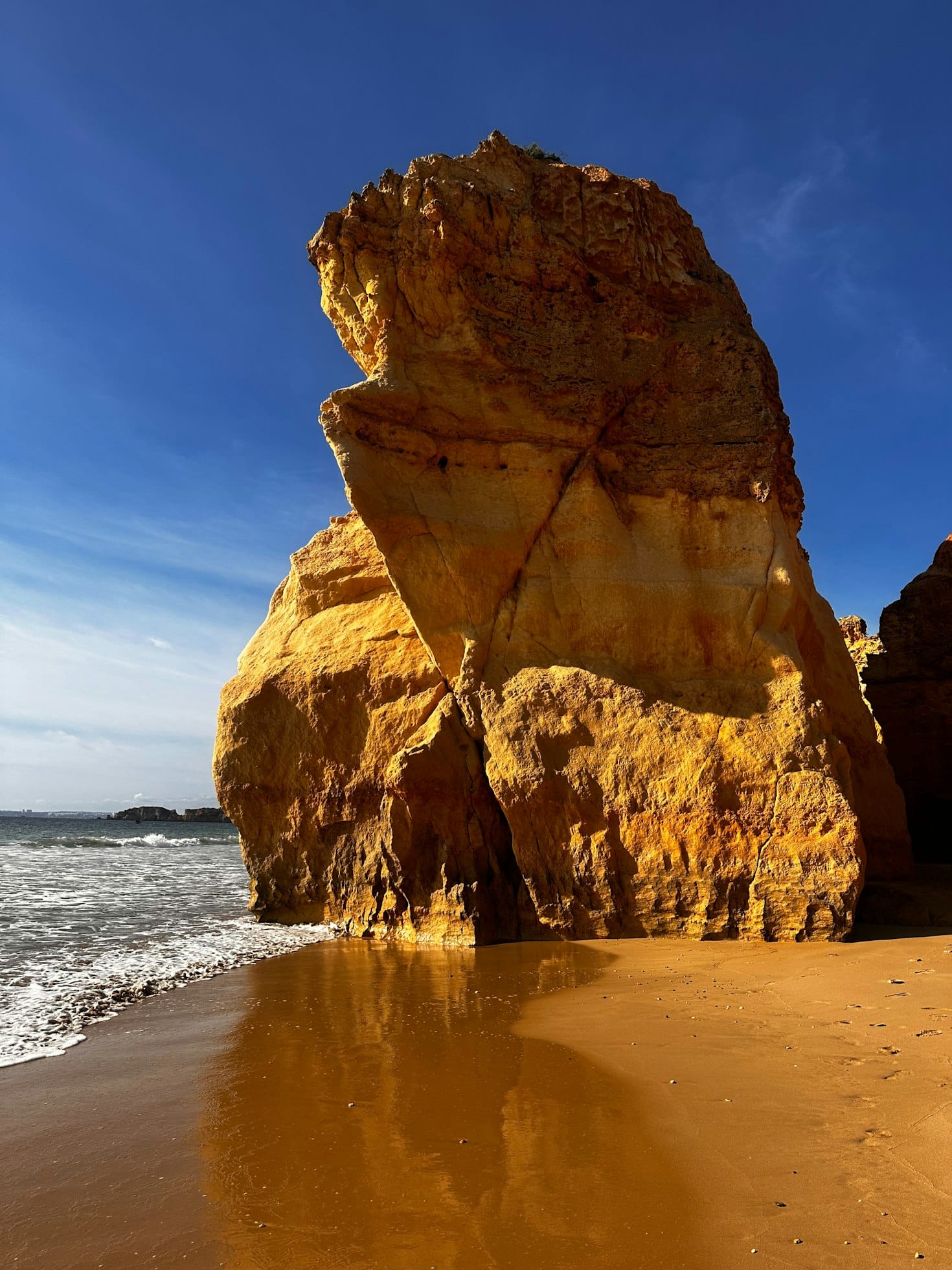 Grande formação rochosa dourada na Praia da Rocha, em Portimão, uma praia arenosa com ondas a aproximar-se sob um céu azul claro.
