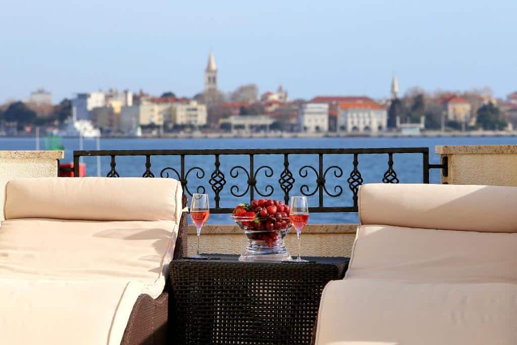 Varanda com vista para o mar e cidade, copos de vinho rosé e travessa com morangos frescos, no Hotel Niko, em Borik