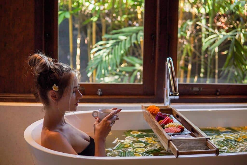 Pessoa a relaxar numa banheira com pétalas de flores e vista para vegetação, num resort em Ubud, Bali.