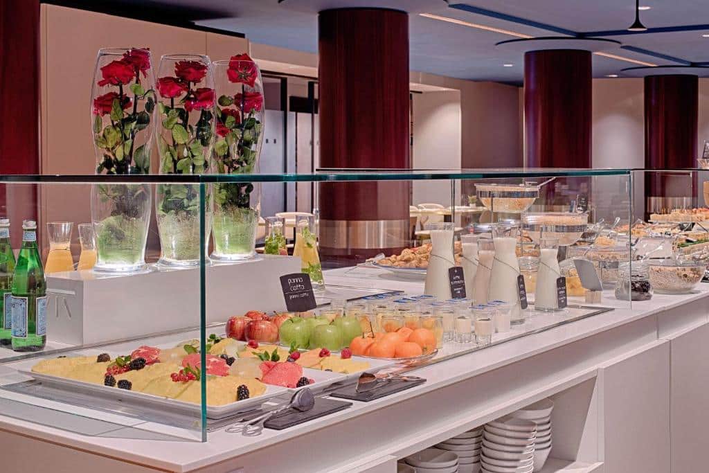 Variedade de sobremesas, fruta fresca e flores num balcão de bufete de um restaurante elegante, no NH Napoli Panorama.