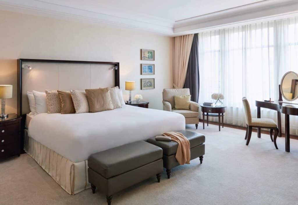 Quarto do Breidenbacher Hof com cama de casal, cómodas com candeeiros e secretária de trabalho. Representa hotéis em Dusseldorf.
