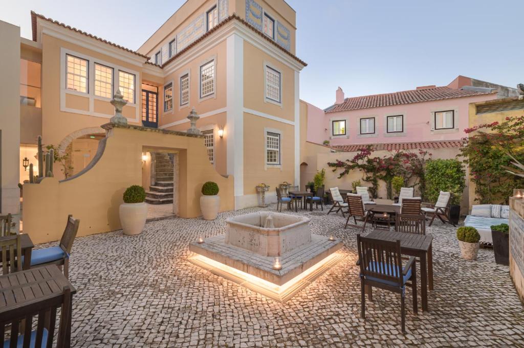 Pátio do Solar do Castelo, com chão de calçada portuguesa, várias cadeiras de madeira, vasos de plantas e iluminação indireta
