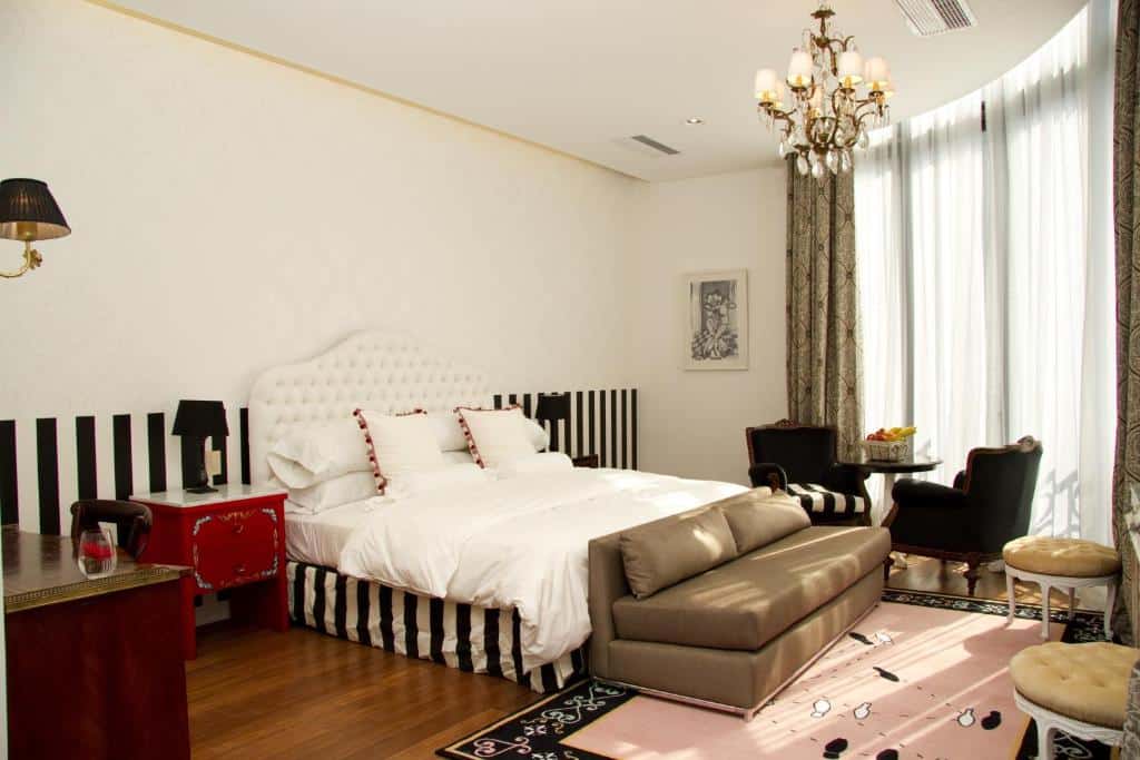 quarto amplo do Tango de Mayo Hotel com cama de casal, sofá em frente a uma tv, candeeiro de teto e janela grande com cortinas em tons suaves com detalhes em vermelho