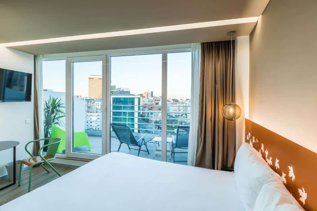 Quarto do Hotel Ibis Styles Lisboa Marquês de Pombal, com cama de casal, varanda, cadeiras, vista para a cidade e janelas grandes que deixam entrar luz natural