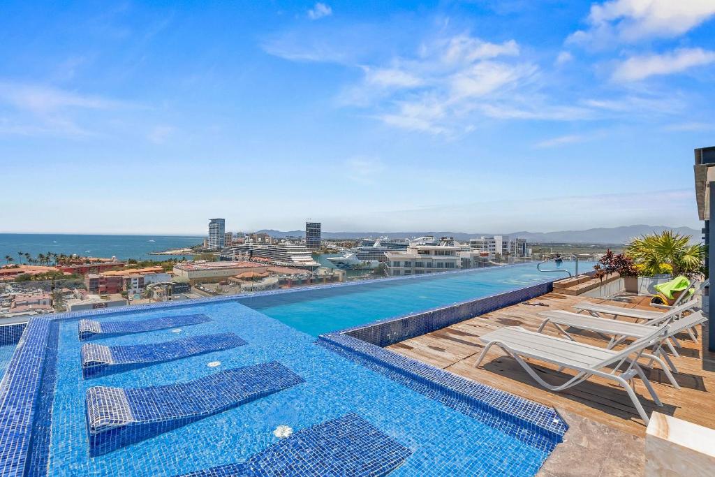 A piscina de borda infinita do Monyxbnb at Zoho Skies com espreguiçadeiras tem vista para a paisagem urbana costeira, a marina e o oceano.