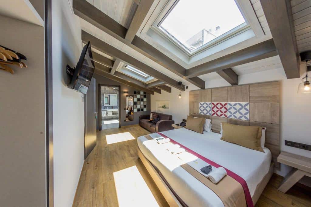 Quarto da Boutique Hostemplo Sagrada Familia. Tem janelas no teto, uma sobre a cama de casal com mesas de cabeceira e outra sobre a zona de estar com sofá, e uma televisão em frente à cama.