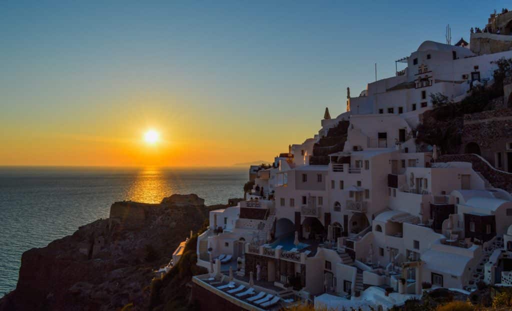 Vista da costa de Oia, em Santorini, com o sol a pôr-se ao fundo