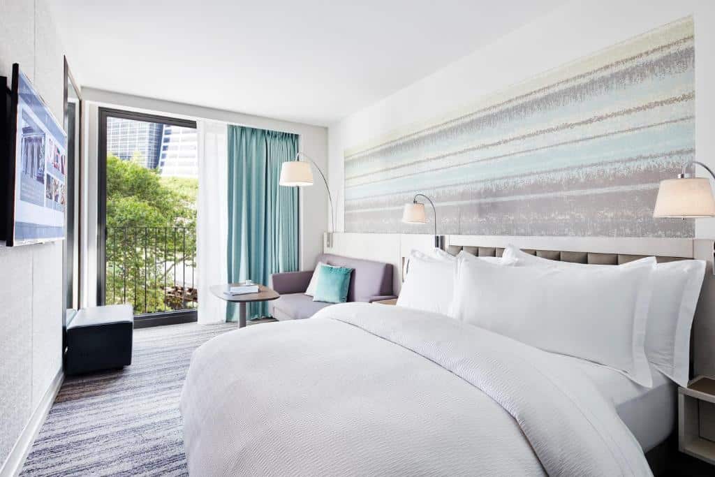 No quarto do Park Terrace Hotel há uma TV na parede à esquerda; ao centro, uma cama de casal com lençóis brancos e, ao lado, um sofá com uma almofada azul. Atrás, uma mesa redonda com cadeira estofada. À direita, cortinados azuis sobre a janela com vista para a cidade.