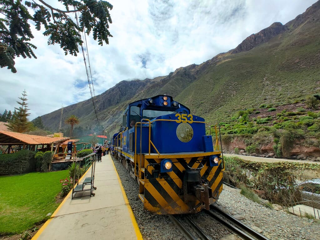 Comboio panorâmico parado na estação de Ollantaytambo, rodeado pelas montanhas peruanas, no Vale Sagrado dos Incas