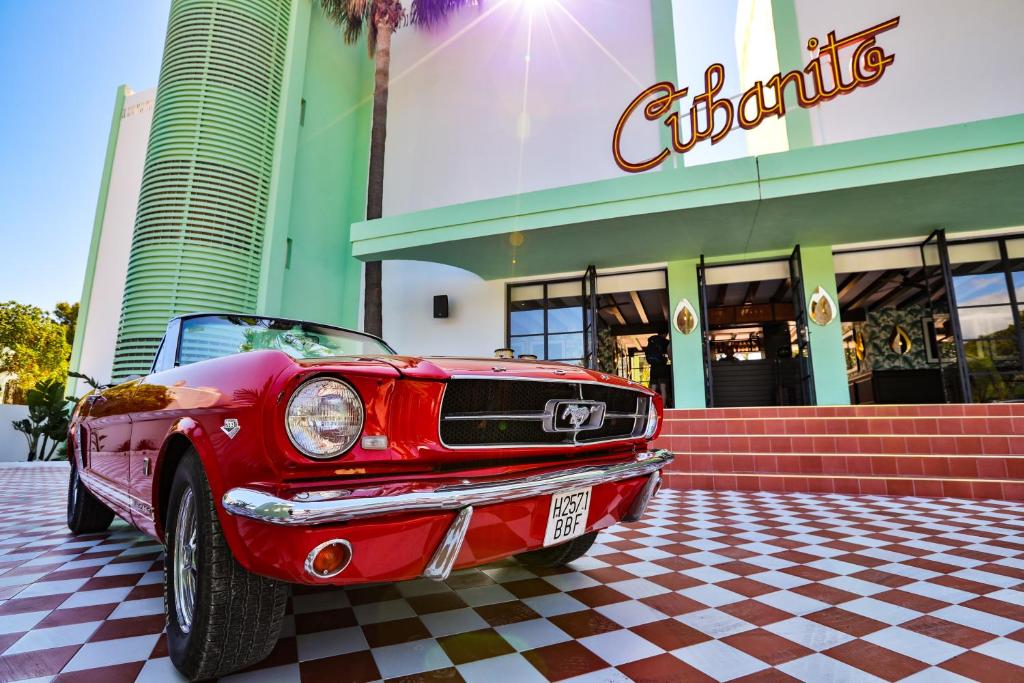 Ford Mustang clássico vermelho estacionado sobre mosaico xadrez em frente à fachada do Cubanito Ibiza.