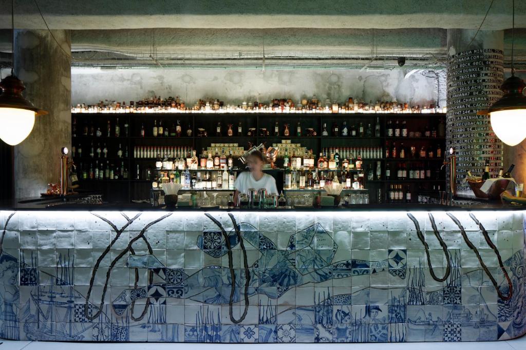 Bar do Zero Box Lodge Porto com balcão e, ao fundo, um funcionário e as bebidas.
